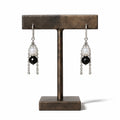Black Tourmaline & Moonstone Earrings — faceted black tourmaline beneath a moonstone in a silver chain cradle, on a bronze earring stand
