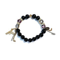 Black stretch bracelet with violet and smoky Austrian crystals, gold pavé rondelles and a gold cross bead, a gold pavé pistol charm and gold and silver chain tassels
